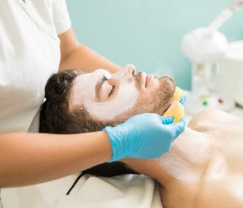 Female therapist washing the face of a male customer while giving a facial in a spa